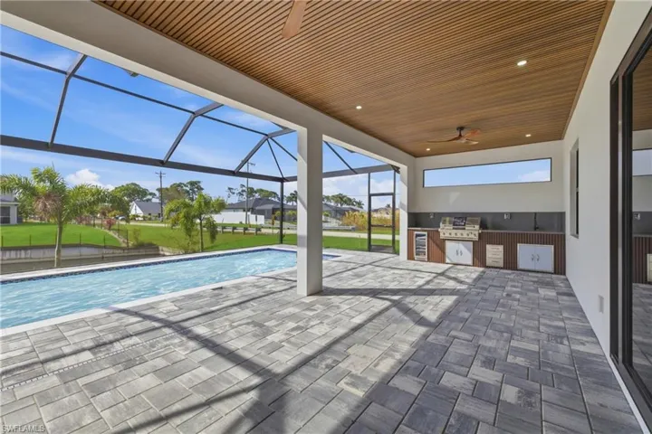 Swimming pool with exterior kitchen, a sunroom, a lawn, a patio area, and a lanai