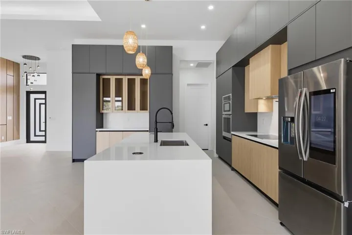 Kitchen with dual tone cabinetry, stainless steel appliances, modern cabinets, a kitchen island with sink, and decorative light fixtures