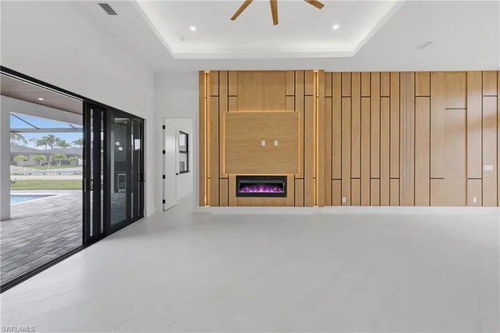 Unfurnished living room with a ceiling fan, a glass covered fireplace, and a high tray ceiling