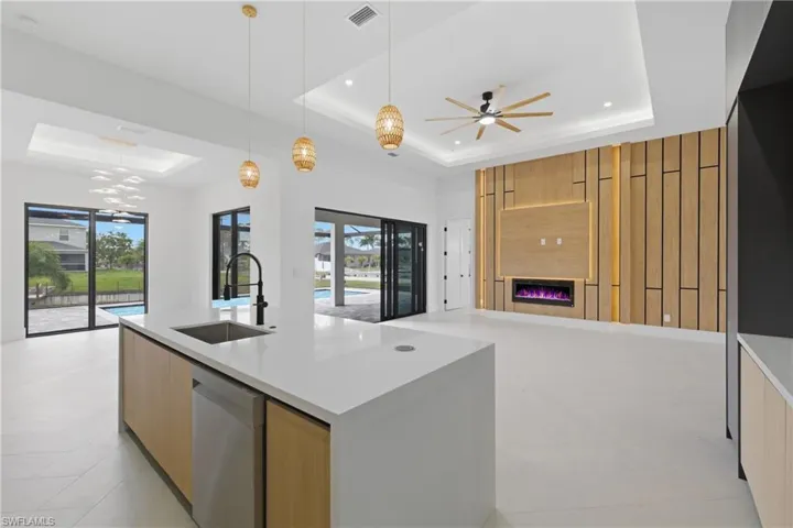 Kitchen featuring open floor plan, a center island with sink, light wood finish cabinetry, decorative light fixtures, and modern cabinets