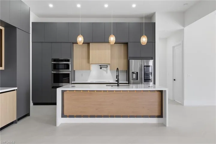 Kitchen featuring modern cabinets, two tone cabinetry, light stone countertops, stainless steel appliances, and a center island with sink