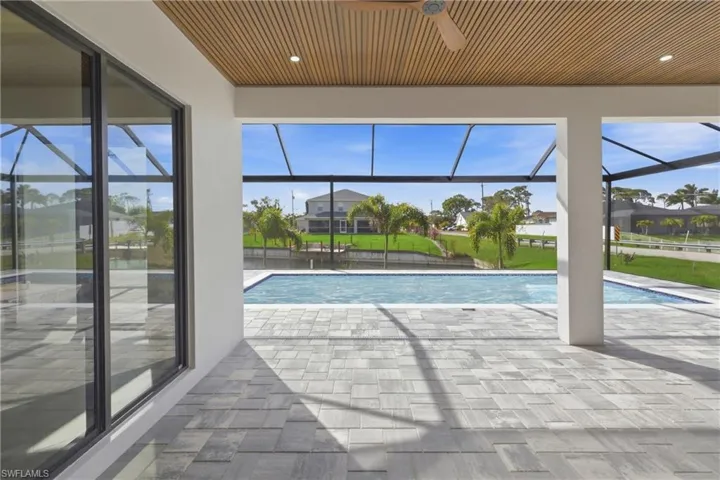 Outdoor pool with a sunroom, a patio area, glass enclosure, and a water view