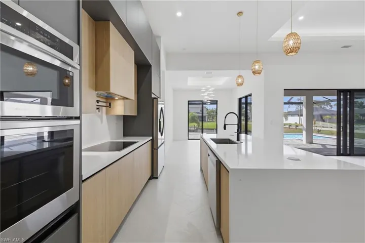 Kitchen featuring stainless steel appliances, a center island with sink, light wood finish cabinets, a tray ceiling, and modern cabinets