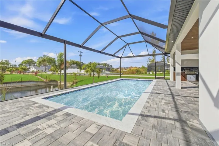 Swimming pool featuring a sunroom, a lanai, a patio area, a lawn, and area for grilling