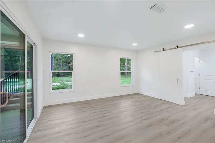 Empty room with a barn door, light wood-style floors, and recessed lighting