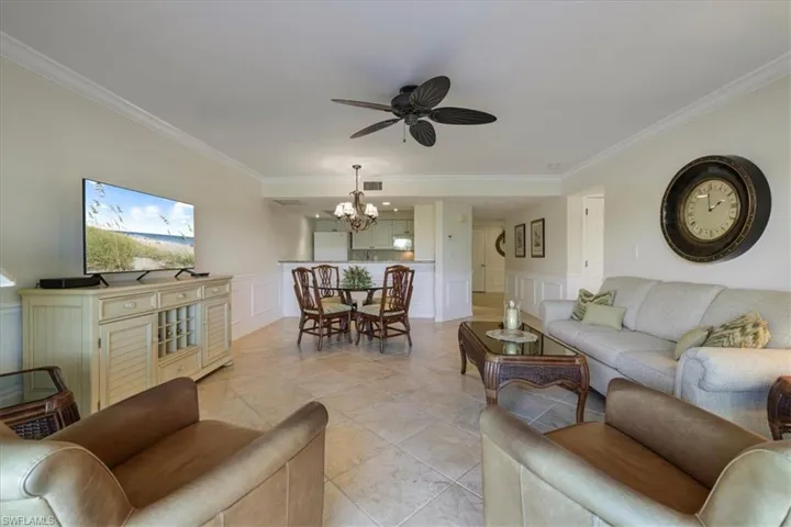 Living area with a decorative wall, wainscoting, crown molding, a ceiling fan, and light tile patterned floors