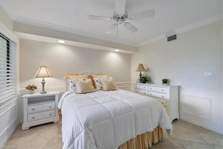 Bedroom with a decorative wall, a wainscoted wall, crown molding, and a ceiling fan