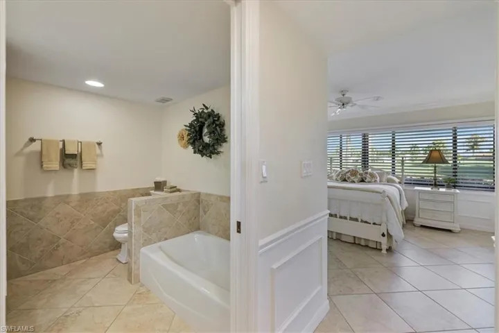 Bathroom featuring a wainscoted wall, light tile patterned floors, a garden tub, a ceiling fan, and ensuite bathroom