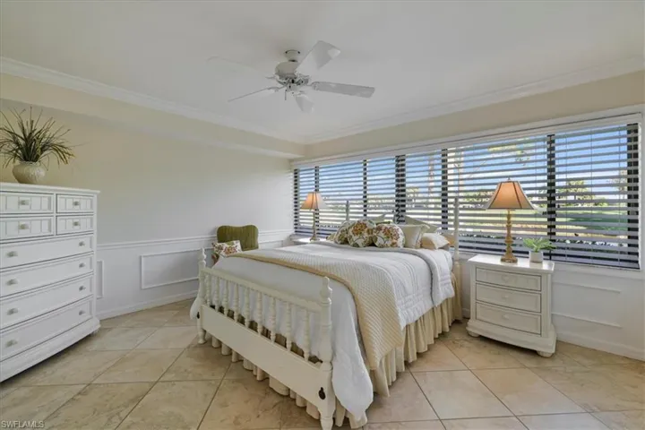 Bedroom featuring a decorative wall, wainscoting, crown molding, a ceiling fan, and light tile patterned flooring