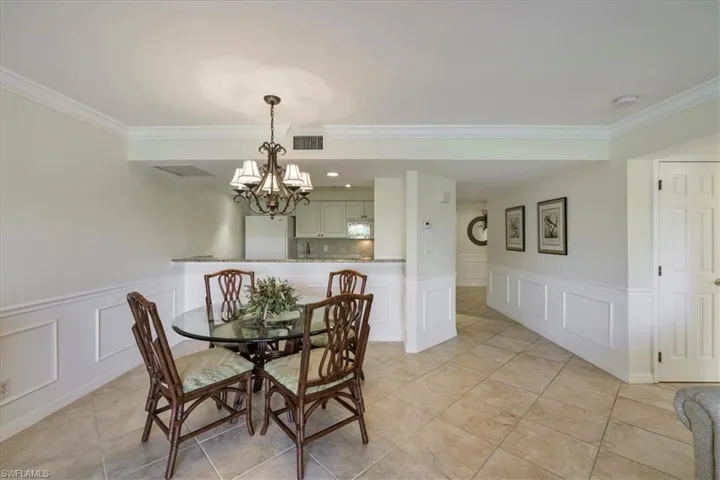 Dining area featuring a decorative wall, a wainscoted wall, a chandelier, crown molding, and light tile patterned flooring