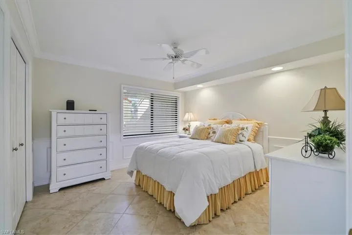Bedroom with a wainscoted wall, a closet, ornamental molding, a ceiling fan, and light tile patterned flooring