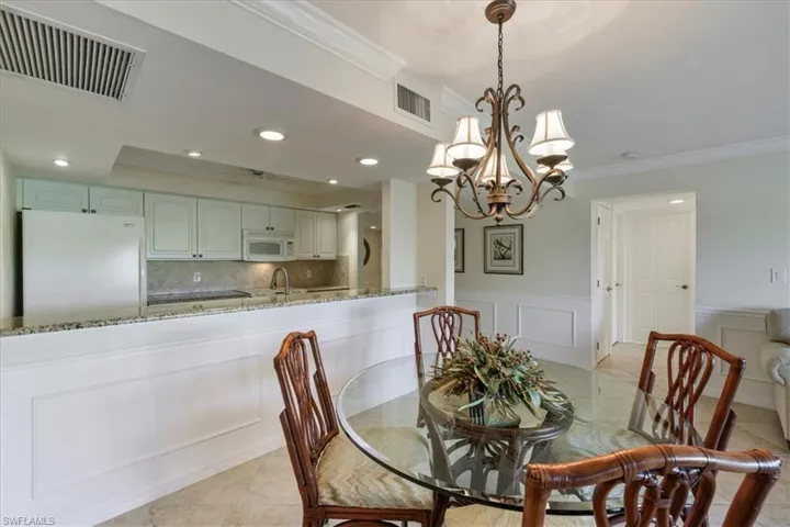Dining room with crown molding, light tile patterned floors, a decorative wall, a chandelier, and wainscoting