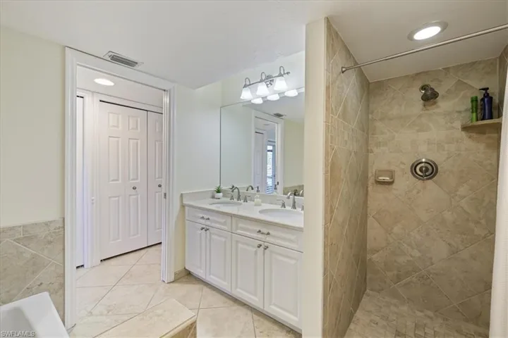 Full bathroom featuring double vanity, a tile shower, recessed lighting, and light tile patterned flooring