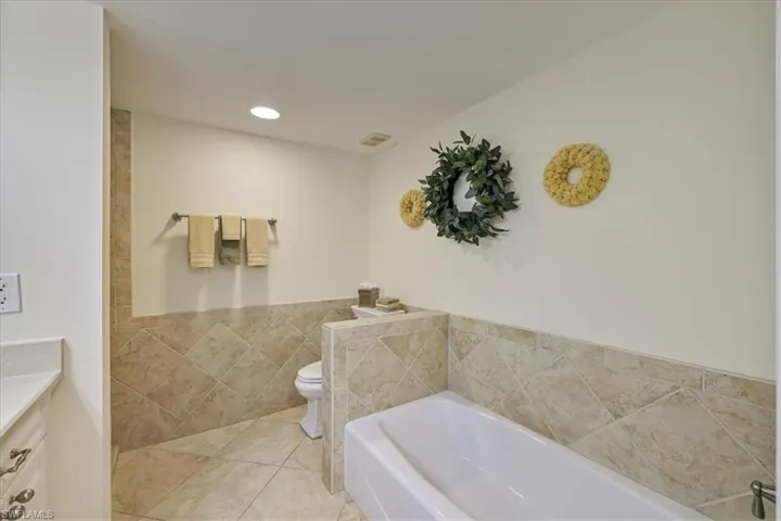 Full bathroom with a garden tub, vanity, recessed lighting, tile walls, and wainscoting