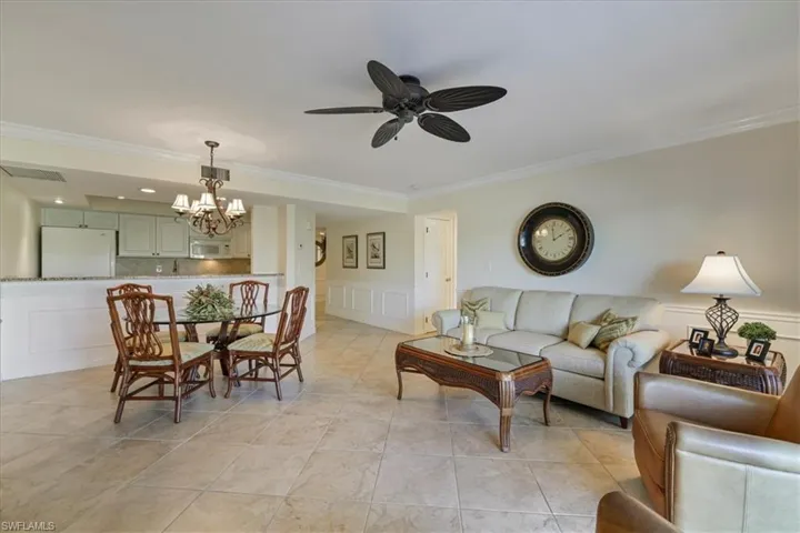 Living area featuring crown molding, a decorative wall, ceiling fan, light tile patterned floors, and wainscoting