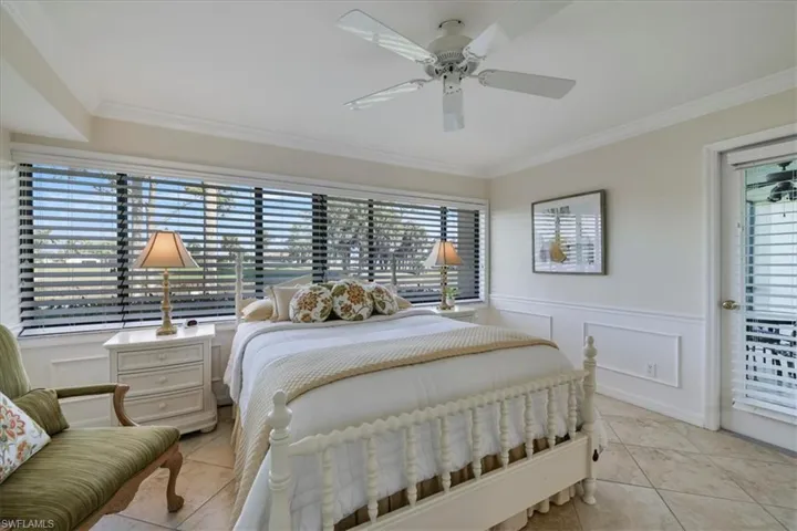 Bedroom with a decorative wall, wainscoting, ornamental molding, ceiling fan, and light tile patterned floors