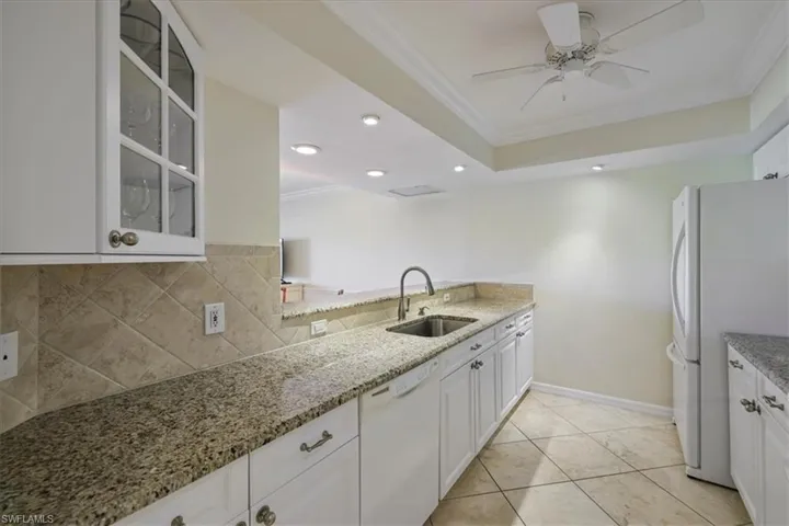 Kitchen featuring ornamental molding, white cabinetry, white appliances, light stone countertops, and glass insert cabinets