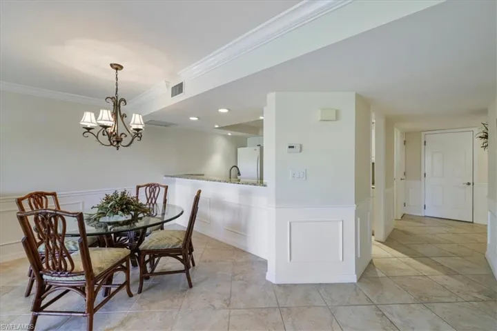 Dining area with wainscoting, a decorative wall, ornamental molding, a chandelier, and light tile patterned flooring