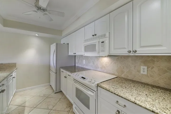 Kitchen with white appliances, white cabinetry, decorative backsplash, crown molding, and light stone countertops