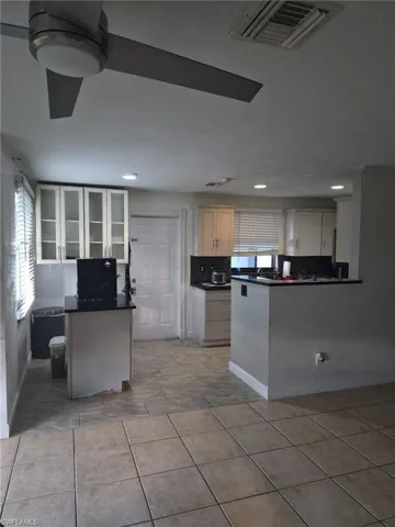 Kitchen with a peninsula, dark countertops, backsplash, glass insert cabinets, and light tile patterned floors