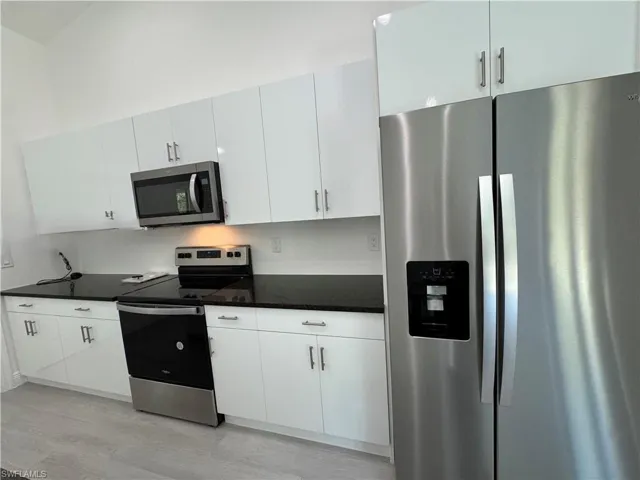 Kitchen with appliances with stainless steel finishes, white cabinetry, dark stone counters, and light wood-style flooring