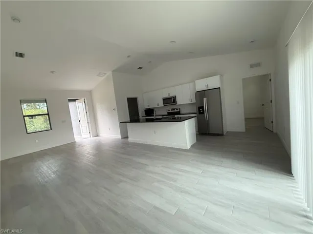 Kitchen featuring open floor plan, appliances with stainless steel finishes, white cabinetry, dark countertops, and a center island with sink