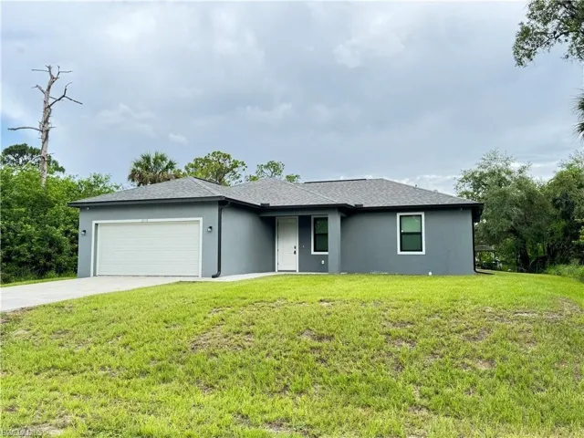 View of front facade featuring stucco siding, concrete driveway, an attached garage, and a front lawn