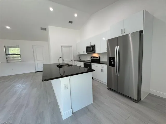 Kitchen featuring stainless steel appliances, white cabinetry, a kitchen island with sink, recessed lighting, and high vaulted ceiling