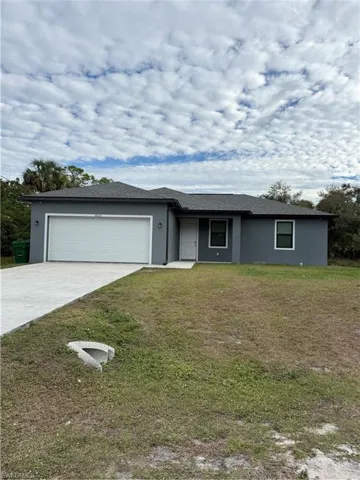 Ranch-style house with stucco siding, driveway, a front lawn, and a garage