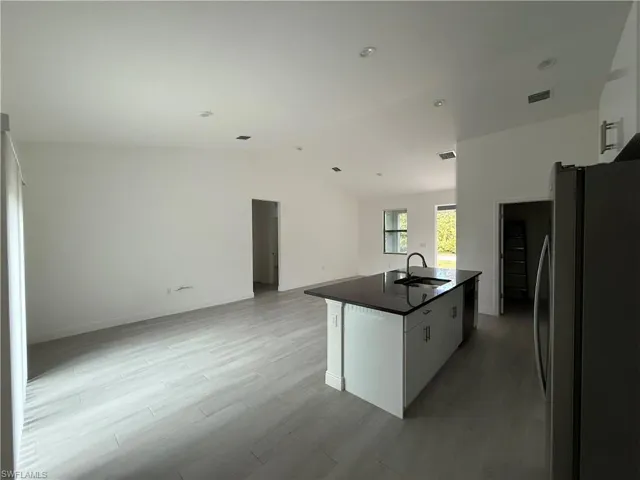 Kitchen with freestanding refrigerator, vaulted ceiling, open floor plan, an island with sink, and white cabinets