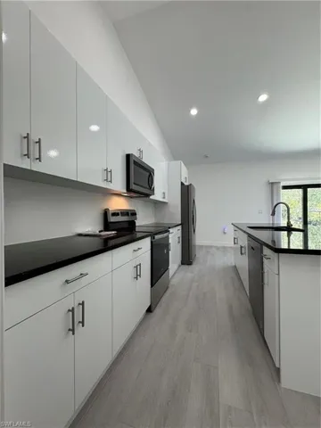 Kitchen with stainless steel appliances, light wood finished floors, recessed lighting, white cabinetry, and dark stone counters