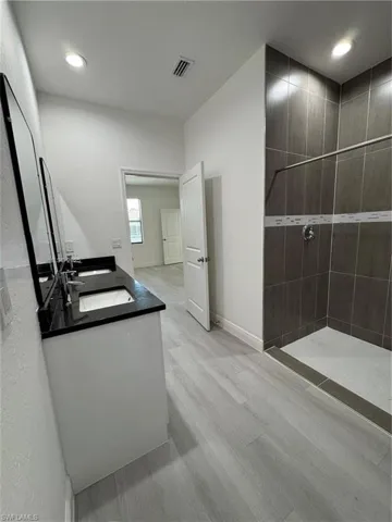 Bathroom featuring double vanity, walk in shower, light wood finished floors, and recessed lighting