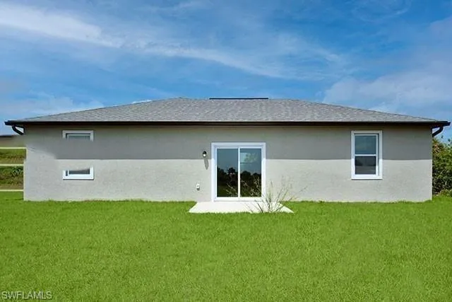 Rear view of house featuring a yard, stucco siding, and a shingled roof