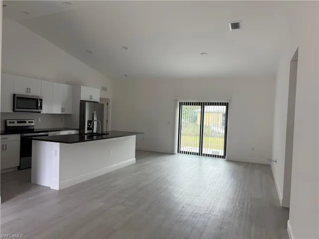 Kitchen featuring appliances with stainless steel finishes, a center island with sink, open floor plan, light wood finished floors, and white cabinetry
