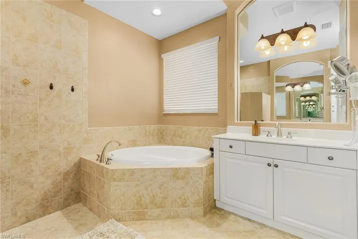 Bathroom featuring a relaxing tiled tub, vanity, and tile patterned floors