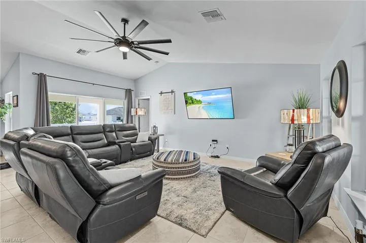 Living room with ceiling fan, light tile patterned floors, and vaulted ceiling