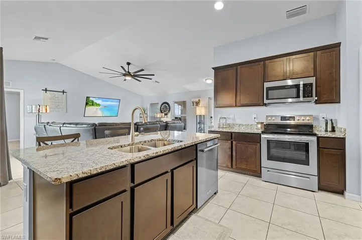 Kitchen featuring dark brown cabinets, stainless steel appliances, sink, lofted ceiling, and light tile patterned flooring