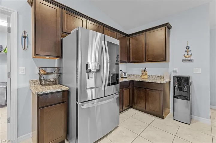 Kitchen featuring lofted ceiling, light stone counters, stainless steel fridge with ice dispenser, and dark brown cabinetry