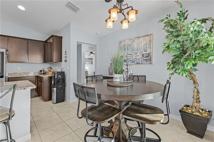 Dining space featuring ceiling fan with notable chandelier, light tile patterned floors, and vaulted ceiling