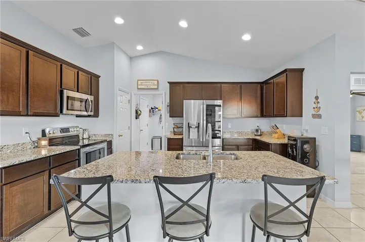 Kitchen with light tile patterned floors, stainless steel appliances, lofted ceiling, and an island with sink