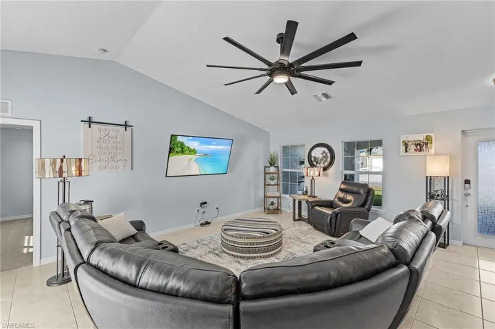 Living room with light tile patterned floors, ceiling fan, and lofted ceiling