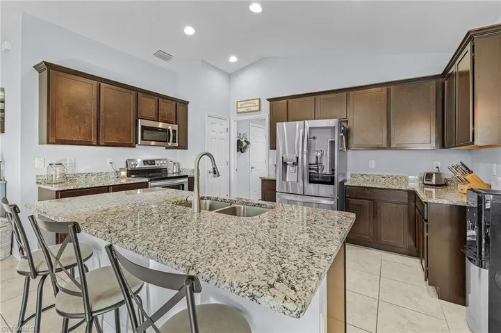 Kitchen with appliances with stainless steel finishes, vaulted ceiling, sink, light tile patterned floors, and a center island with sink
