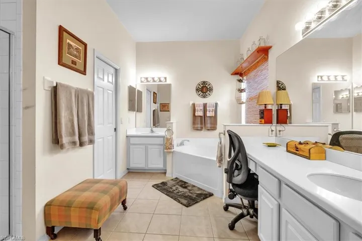 Bathroom featuring two vanities, a stall shower, light tile patterned floors, and a garden tub
