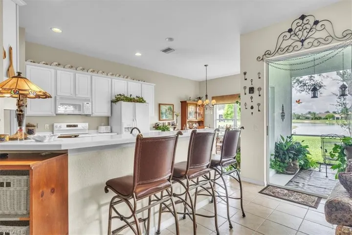 Kitchen with a breakfast bar area, pendant lighting, white appliances, white cabinetry, and a peninsula