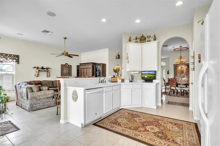 Kitchen featuring light tile patterned floors, a peninsula, arched walkways, white appliances, and white cabinets
