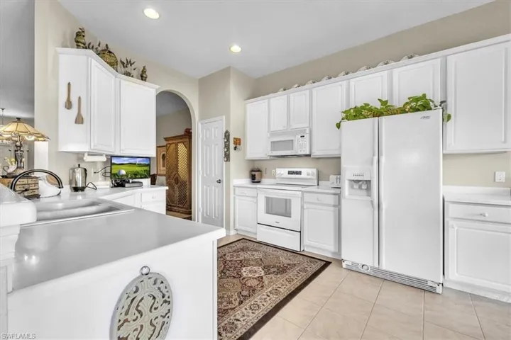 Kitchen with white appliances, arched walkways, white cabinets, light countertops, and light tile patterned floors