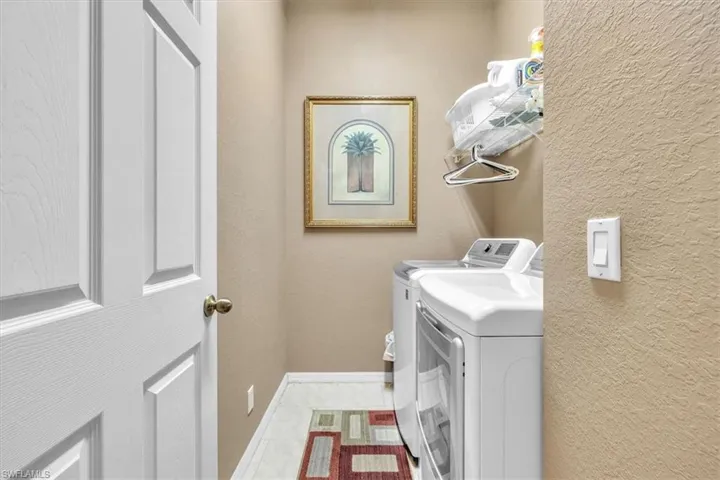 Laundry room with a textured wall, washing machine and clothes dryer, and tile patterned floors