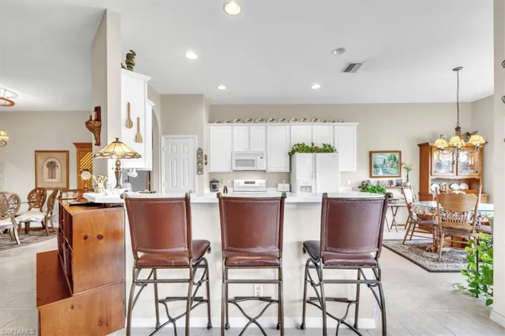 Kitchen featuring a chandelier, hanging light fixtures, a kitchen bar, white appliances, and light countertops