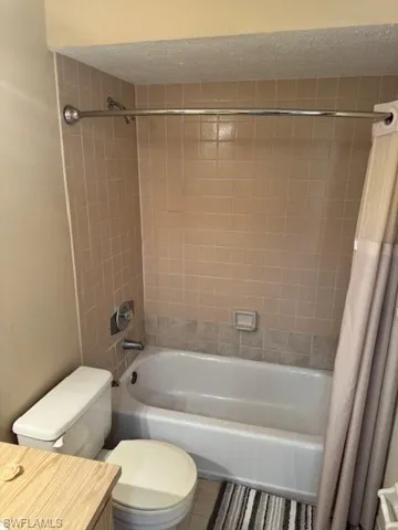 Full bathroom featuring shower / tub combo with curtain, a textured ceiling, tile patterned flooring, and vanity