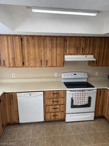 Kitchen with white stove, brown cabinetry, dishwasher, light countertops, and exhaust hood